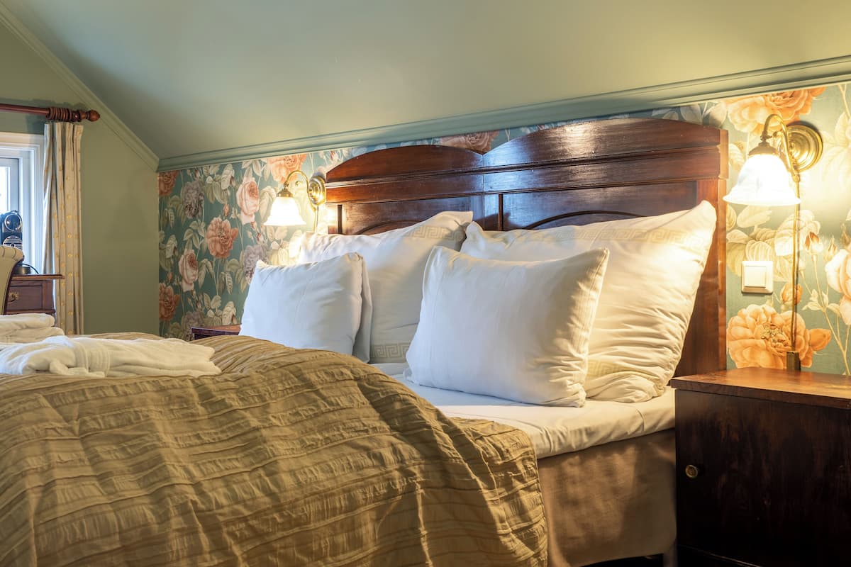 Uma cama bem arrumada com cabeceira de madeira, papel de parede com padrão floral e duas luminárias de cabeceira.