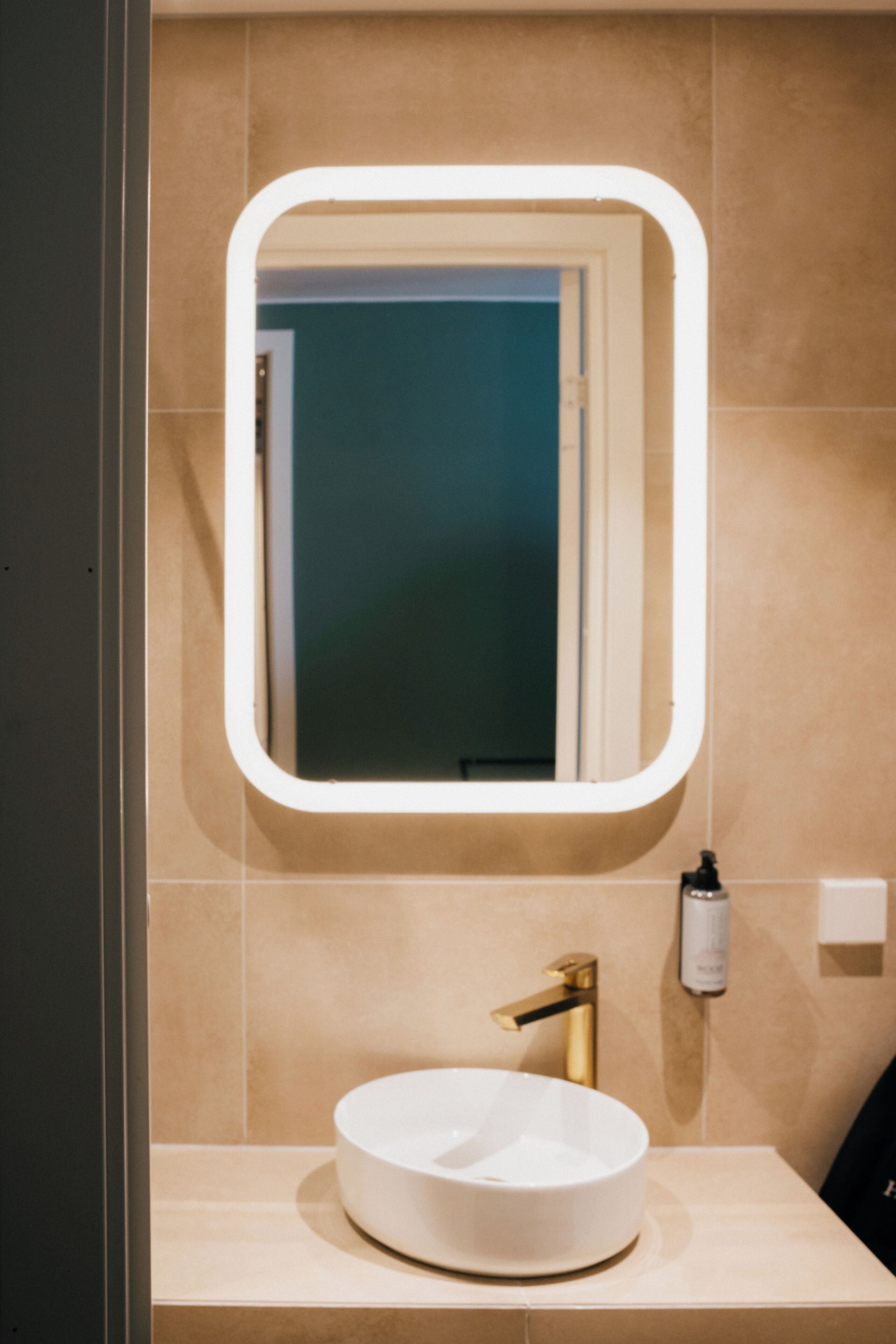 Un baño con un lavabo blanco redondo, un grifo dorado y un espejo con marco blanco.