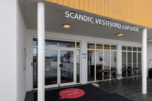 Het uiterlijk van hotel Scandic Vestfjord Lofoten, met een bord boven de ingang, een glazen deur en een zitgedeelte buiten.