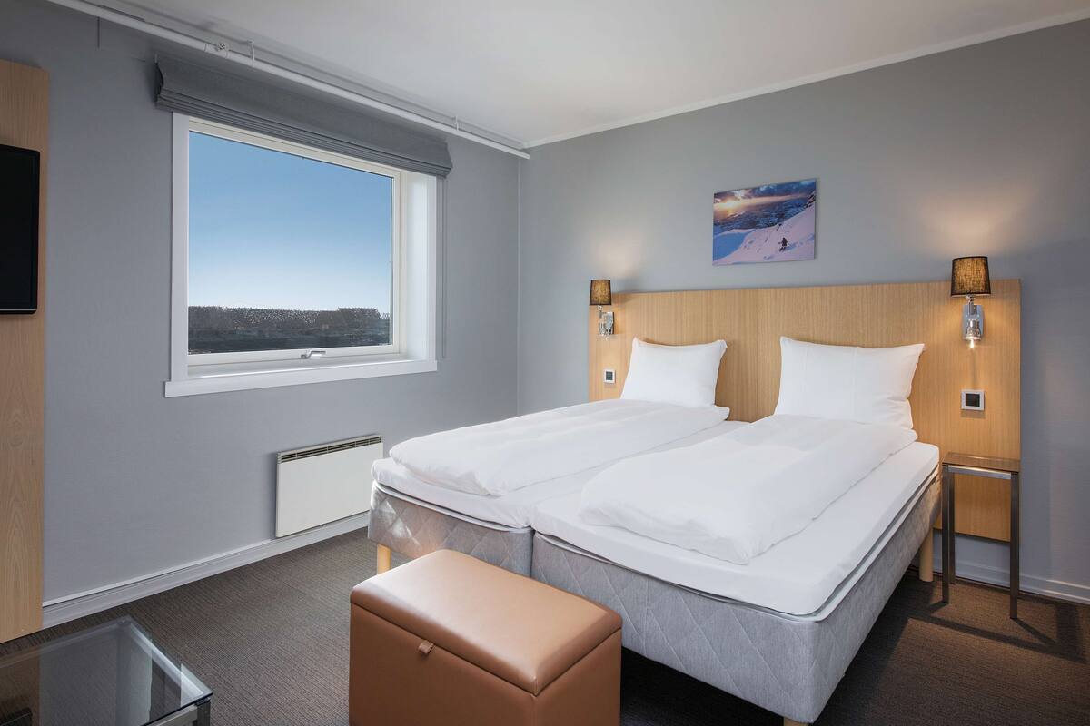 Une chambre d’hôtel avec un grand lit, deux tables de chevet avec des lampes, une fenêtre donnant sur un beau paysage et une petite table avec une chaise.