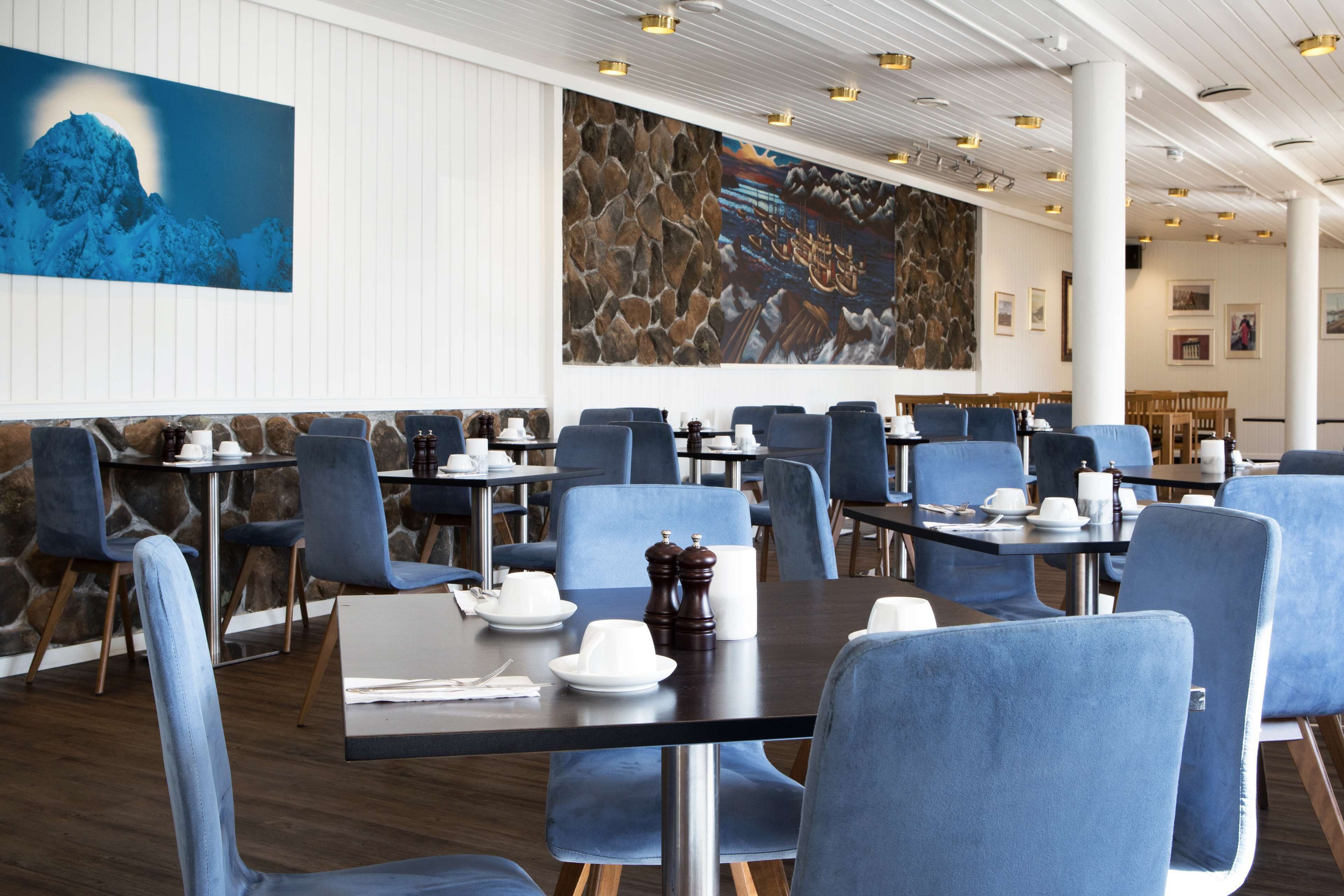A restaurant with blue upholstered chairs, dark tables, and a stone wall.