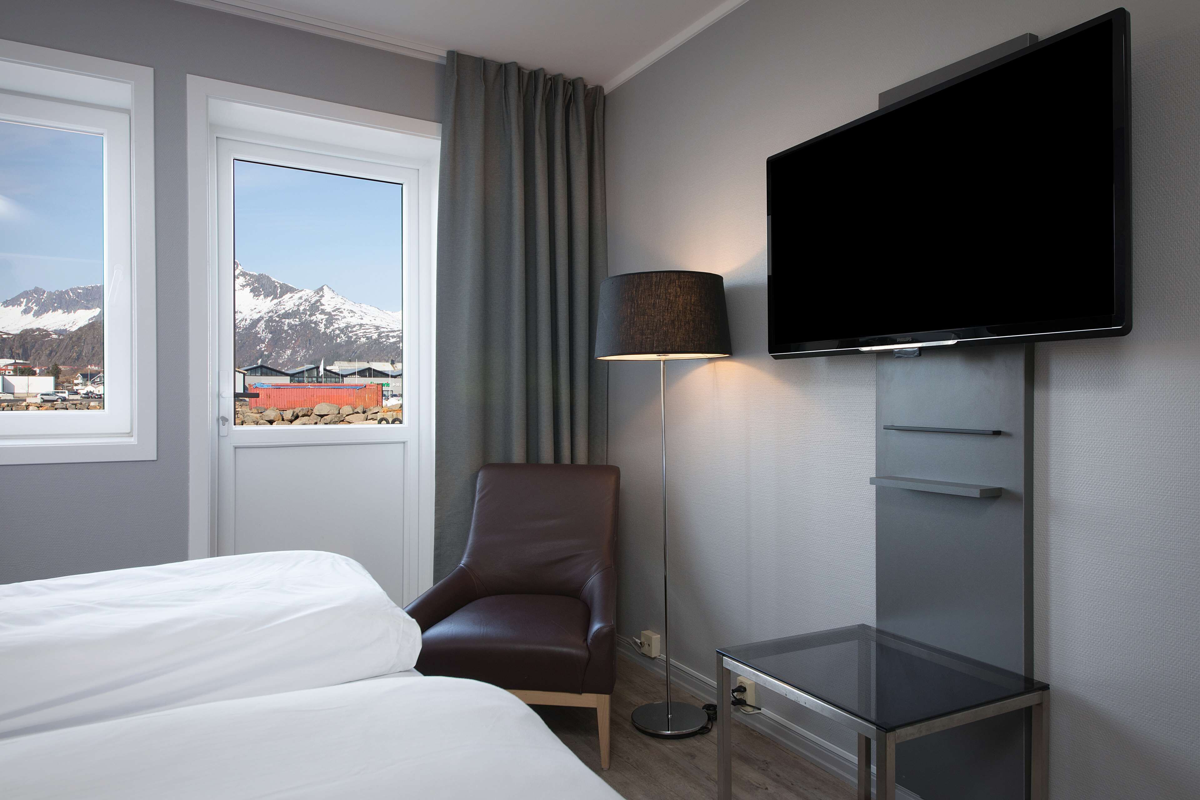 Une chambre d’hôtel avec un lit, une chaise, une télévision et une vue sur les montagnes.