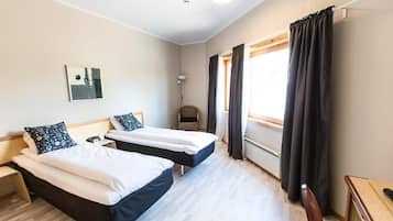 A hotel room with two beds, a bedside table, a lamp, a chair, and a window with curtains.