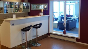 Cozinha moderna com área de bar, bancada branca, dois banquetes e uma janela ampla que dá para uma sala de estar.