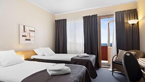 Quarto de hotel com duas camas, uma escrivaninha, uma cadeira e uma varanda com cortinas.