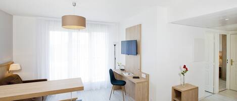 Een moderne hotelkamer met een houten bureau, een blauwe stoel, een klein bijzettafeltje met een vaas en een televisie aan de muur.