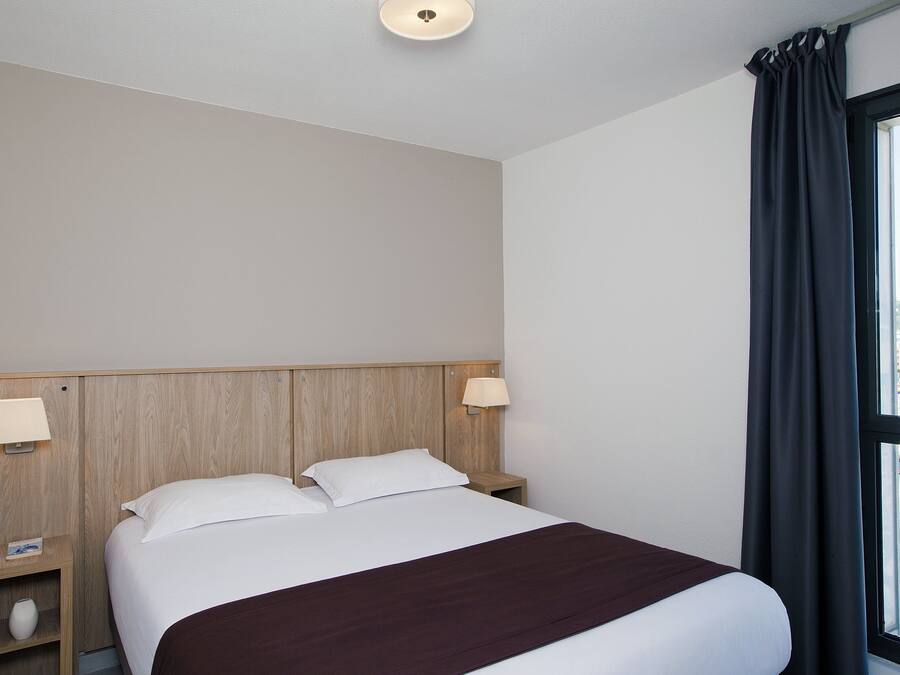 Habitación de hotel con cama, dos lámparas de noche, una mesita de noche y una ventana con cortinas.