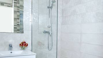 A modern bathroom with a glass-enclosed shower, a white vanity with drawers, and a mirror above the sink.