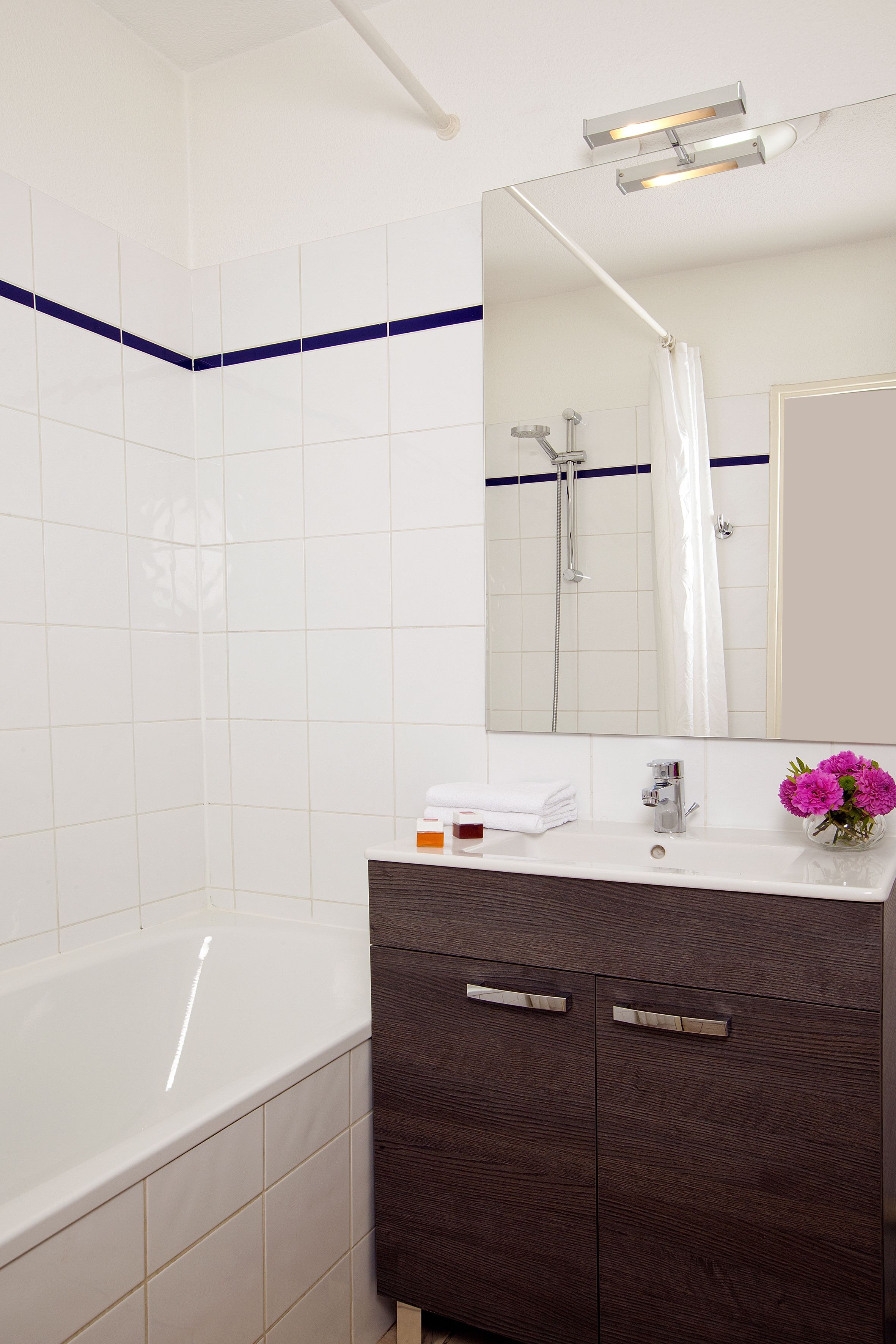 A modern bathroom with a white bathtub, dark wooden vanity, and a large mirror.