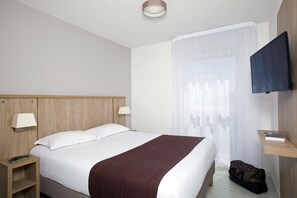 A hotel room with a bed, bedside tables, a TV, and a window with sheer curtains. - Residhome Lyon Gerland (Lyon)