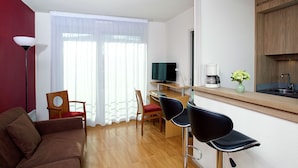 Un espacio habitable compacto con sofá, dos sillones, televisor, cafetera y una pequeña cocina con pileta y alacena.