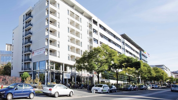 Un hotel de varios pisos con balcones, un restaurante en la planta baja y un estacionamiento.