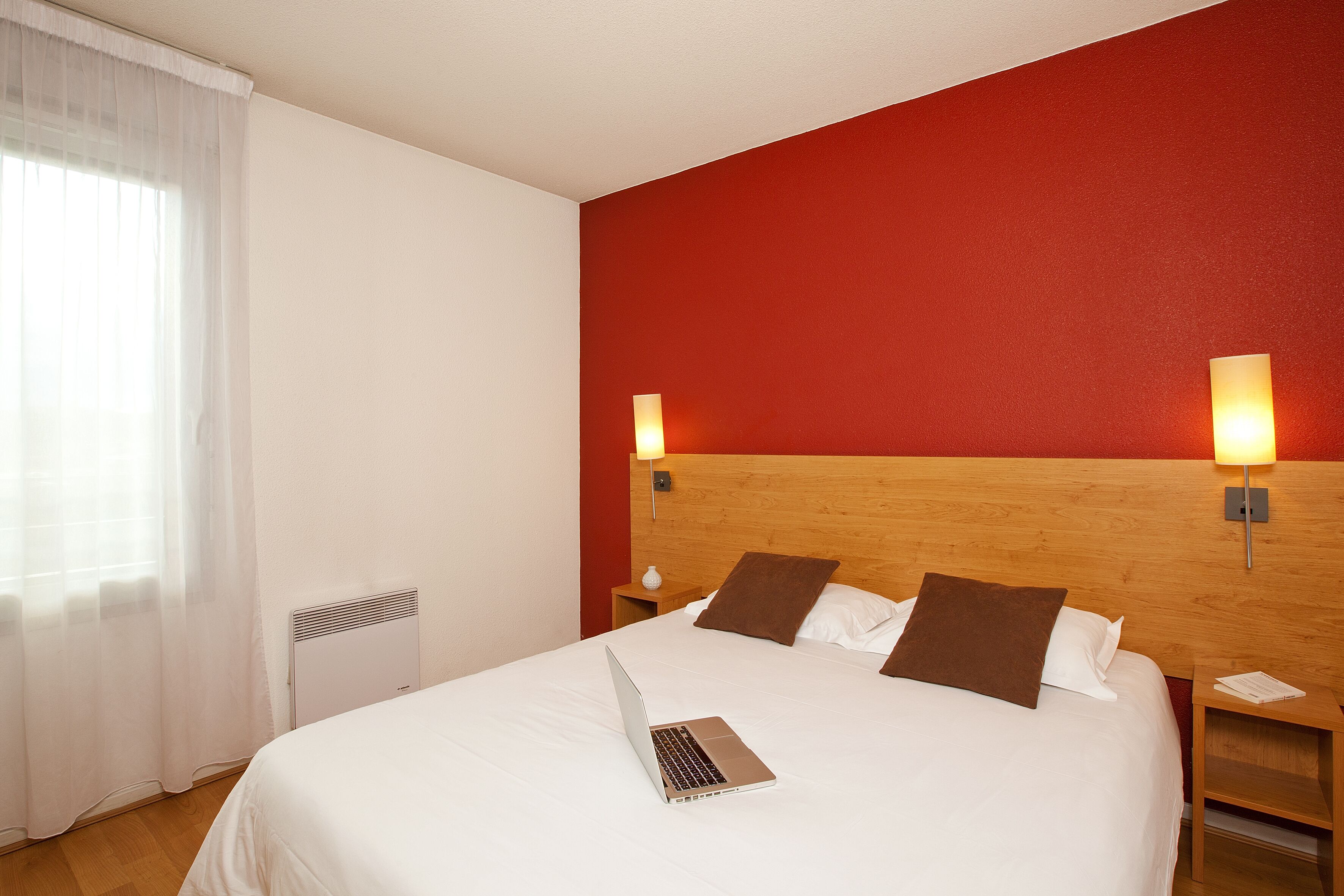 Een hotelkamer met een bed, een laptop, een nachtkastje en een wandlamp.