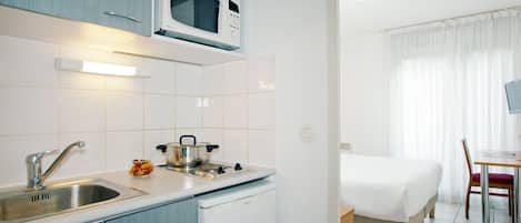 Una kitchenette compacta con microondas, estufa, pileta y heladera pequeña.