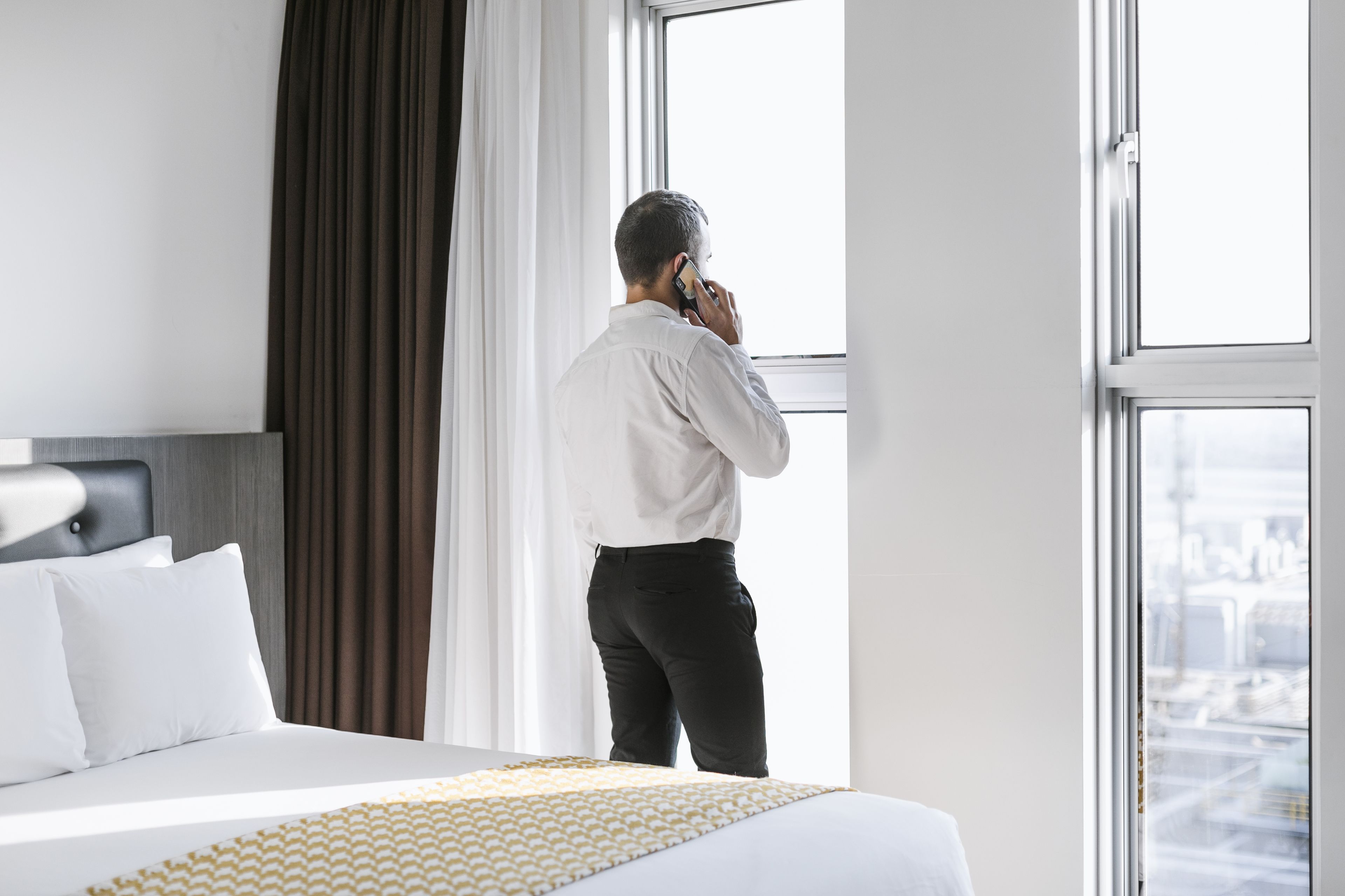 A hotel room with a large bed, a window with curtains, and a city view.