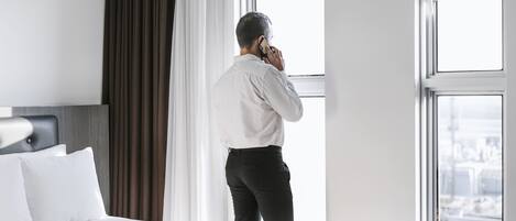 A hotel room with a large bed, a window with curtains, and a city view.
