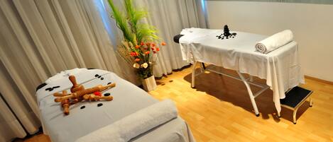 A spa room with a massage table, a foot bath, and a small table with a towel and black stones.