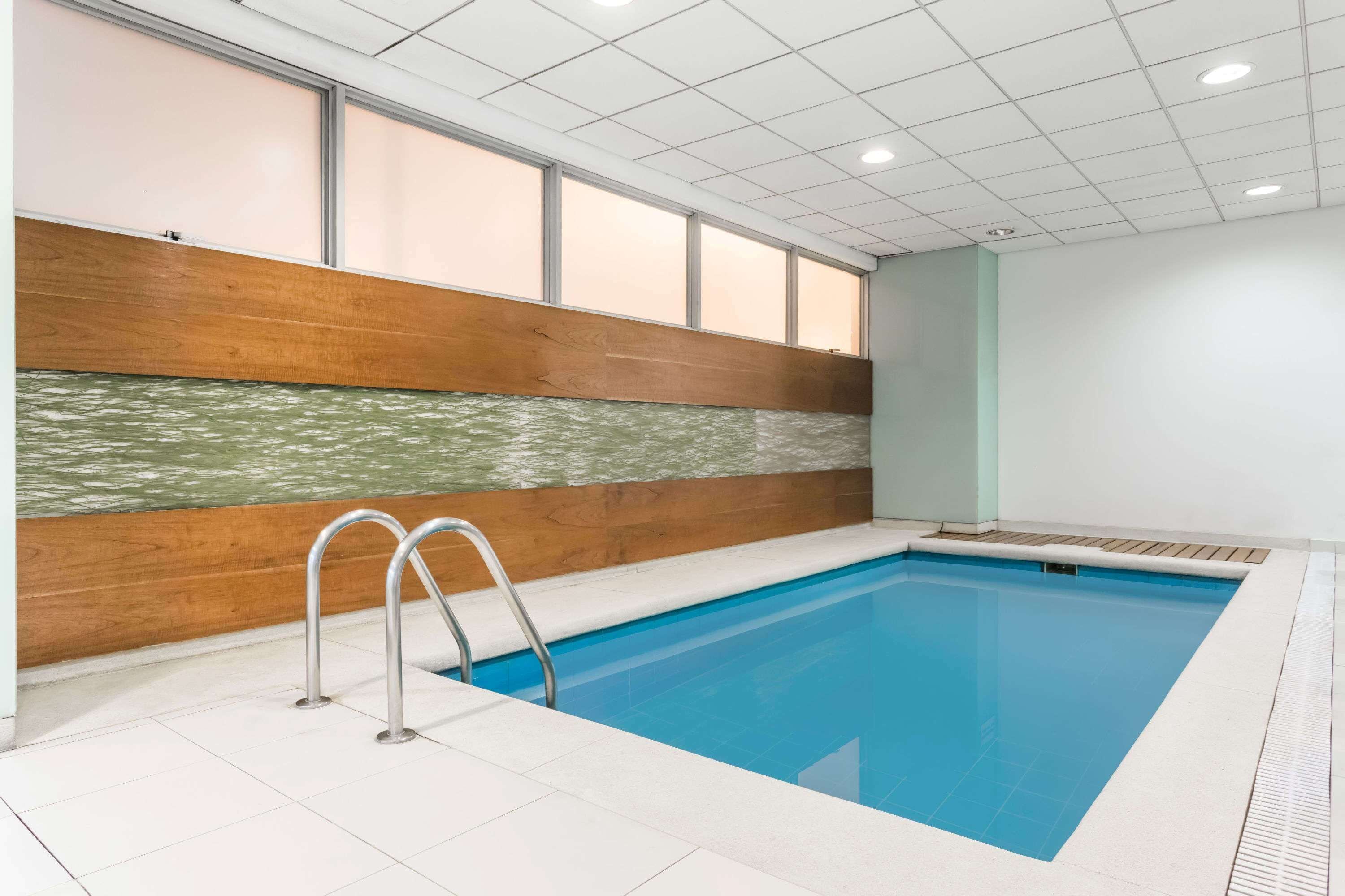 An indoor swimming pool with clear water, a wooden wall with a greenish pattern, and a tiled floor.