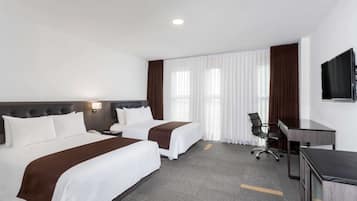 Habitación de hotel con dos camas, un escritorio, una silla y un televisor.