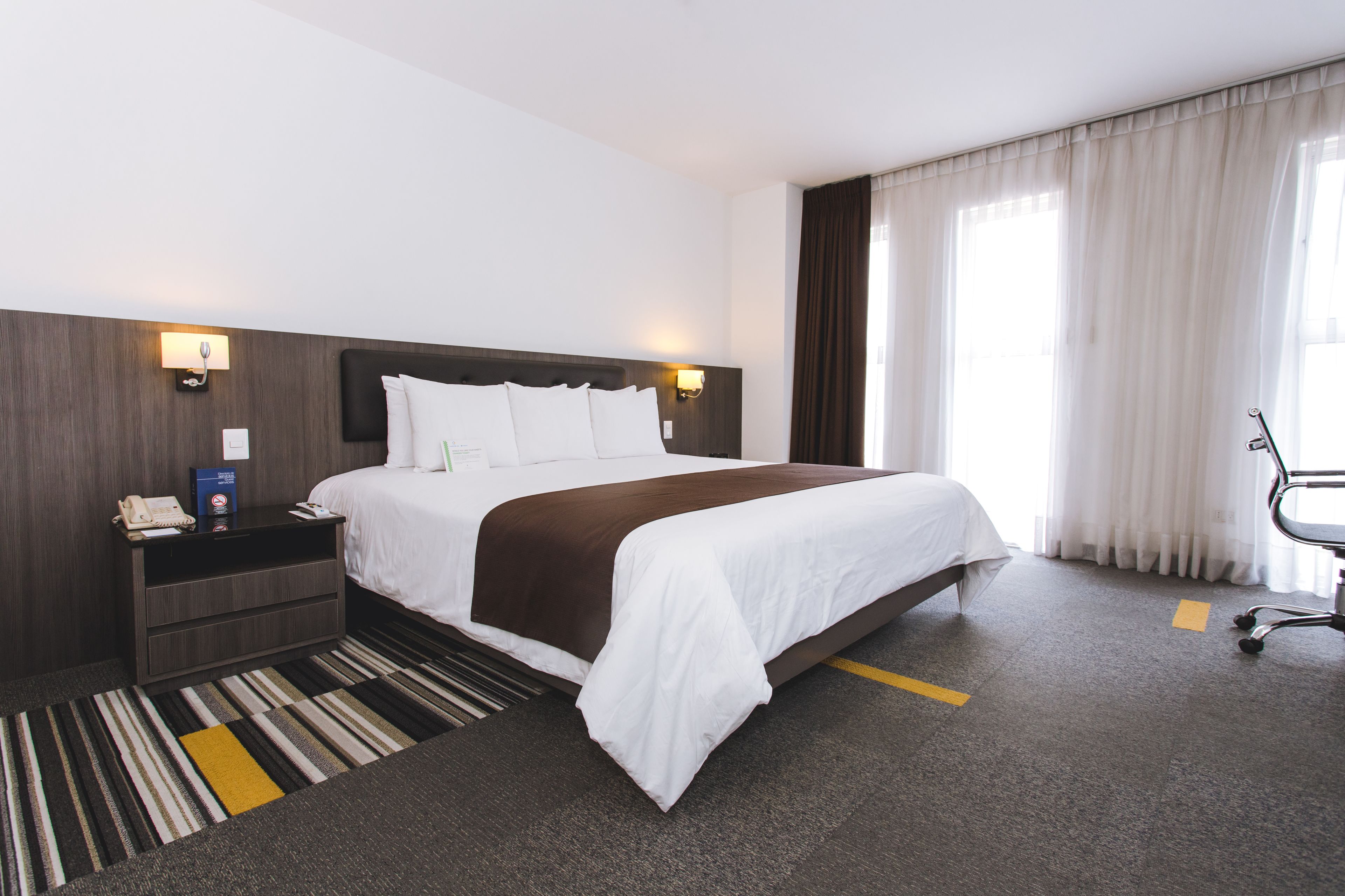 Een hotelkamer met een groot bed, een nachtkastje met een telefoon, een bureaulamp en een stoel.