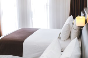 Una cama bien hecha con ropa de cama blanca y marrón, una lámpara de noche y almohadas blancas.