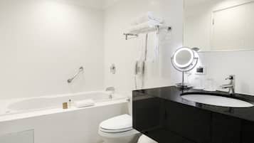 A modern bathroom with a white bathtub, a toilet, a black sink, and a mirror with a light.
