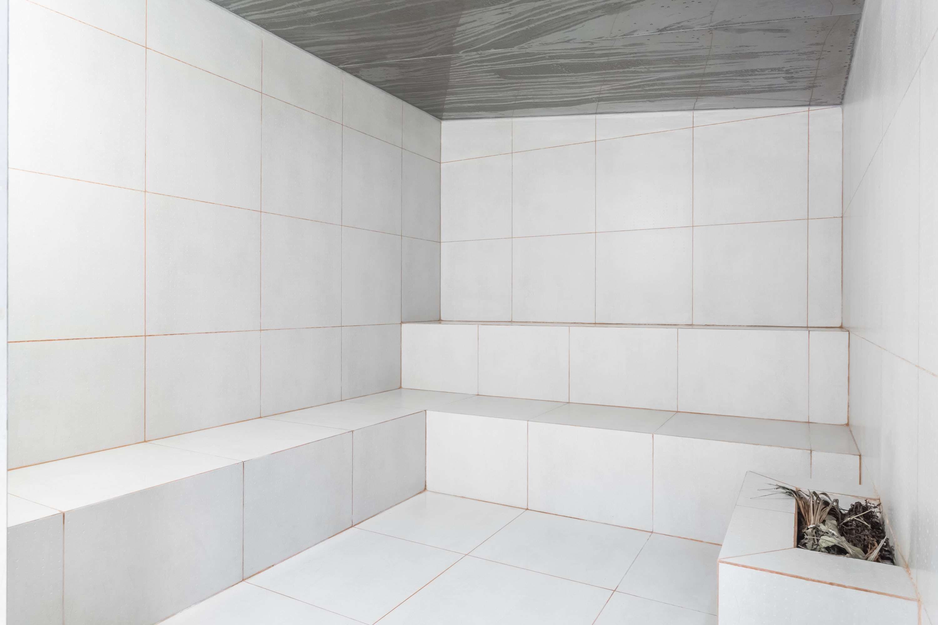 Een moderne badkamer met witte tegels, een ingebouwde bank en een plantje rechts.