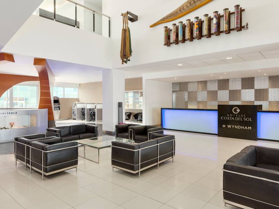 Een moderne hotellobby met zwarte leren banken, een conciërgedesk en een receptie met een incheckbalie.