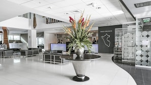 Un moderno vestíbulo de hotel con mostrador de recepción, zona de estar y un jarrón decorativo con flores.