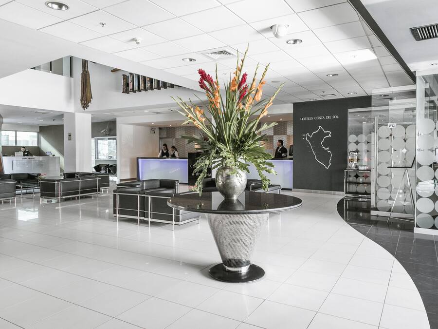 Un moderno vestíbulo de hotel con mostrador de recepción, zona de estar y un jarrón decorativo con flores.
