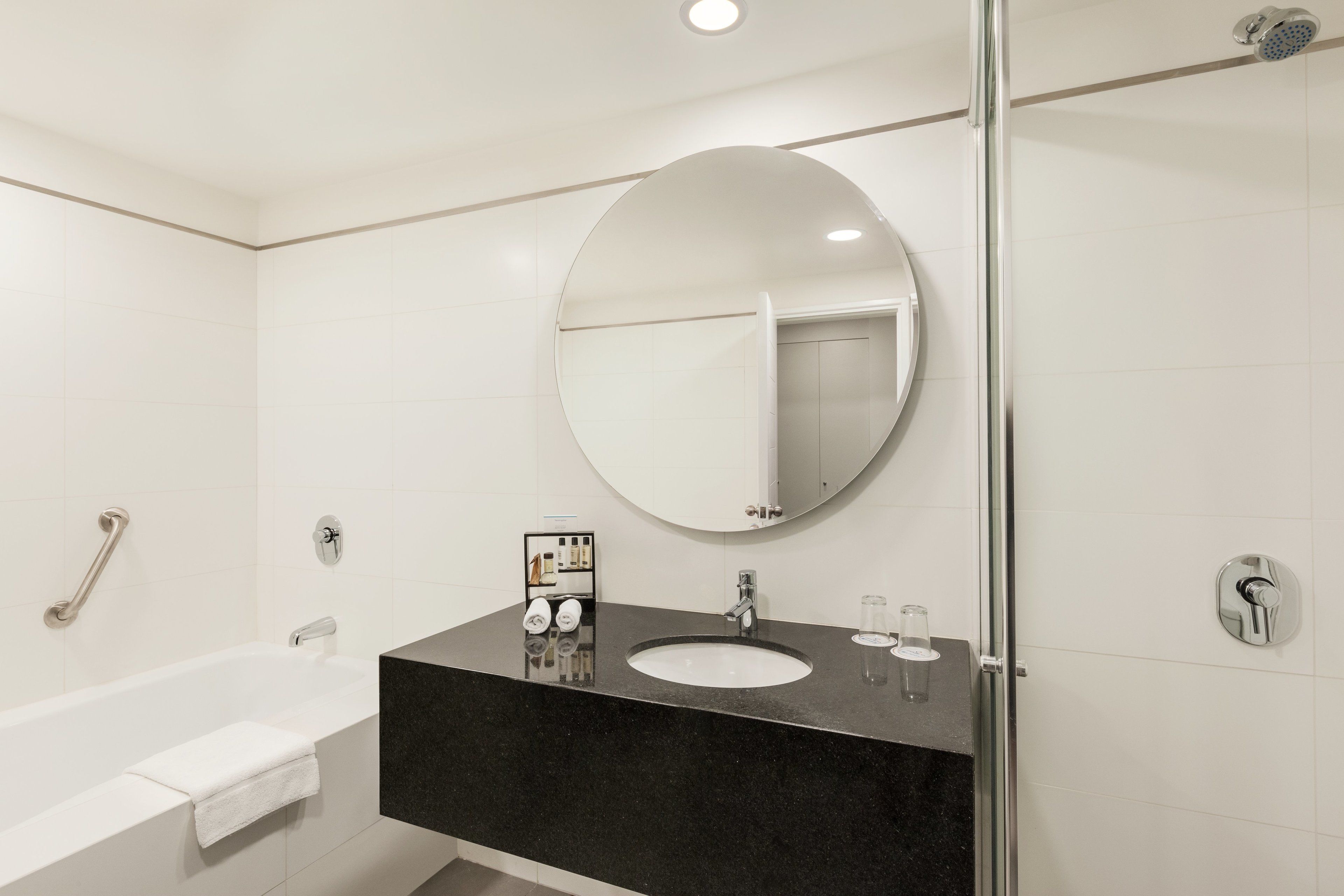 A modern bathroom with a bathtub, a round mirror, a sink, and a glass shower enclosure.