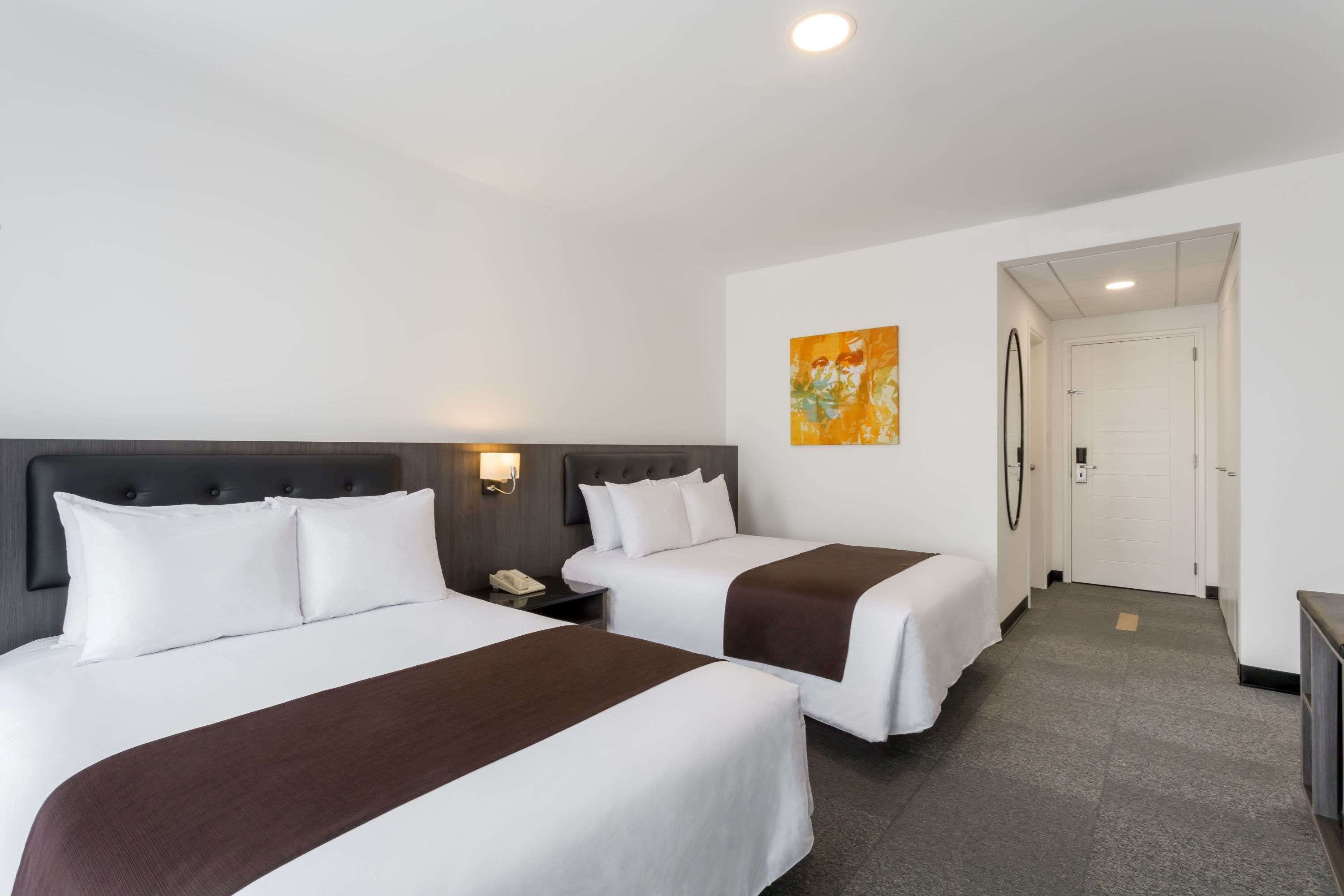 A hotel room with two beds, a nightstand, a painting, and a door leading to another room.