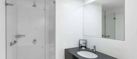 A modern bathroom with a glass shower enclosure, a white sink, and a large mirror.