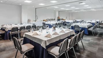 Un salón de conferencias con varias mesas dispuestas para reuniones, equipado con sillas, botellas de agua y placas de identificación.