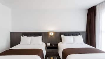 Habitación de hotel con dos camas, una mesita de noche, una lámpara y vistas al exterior.