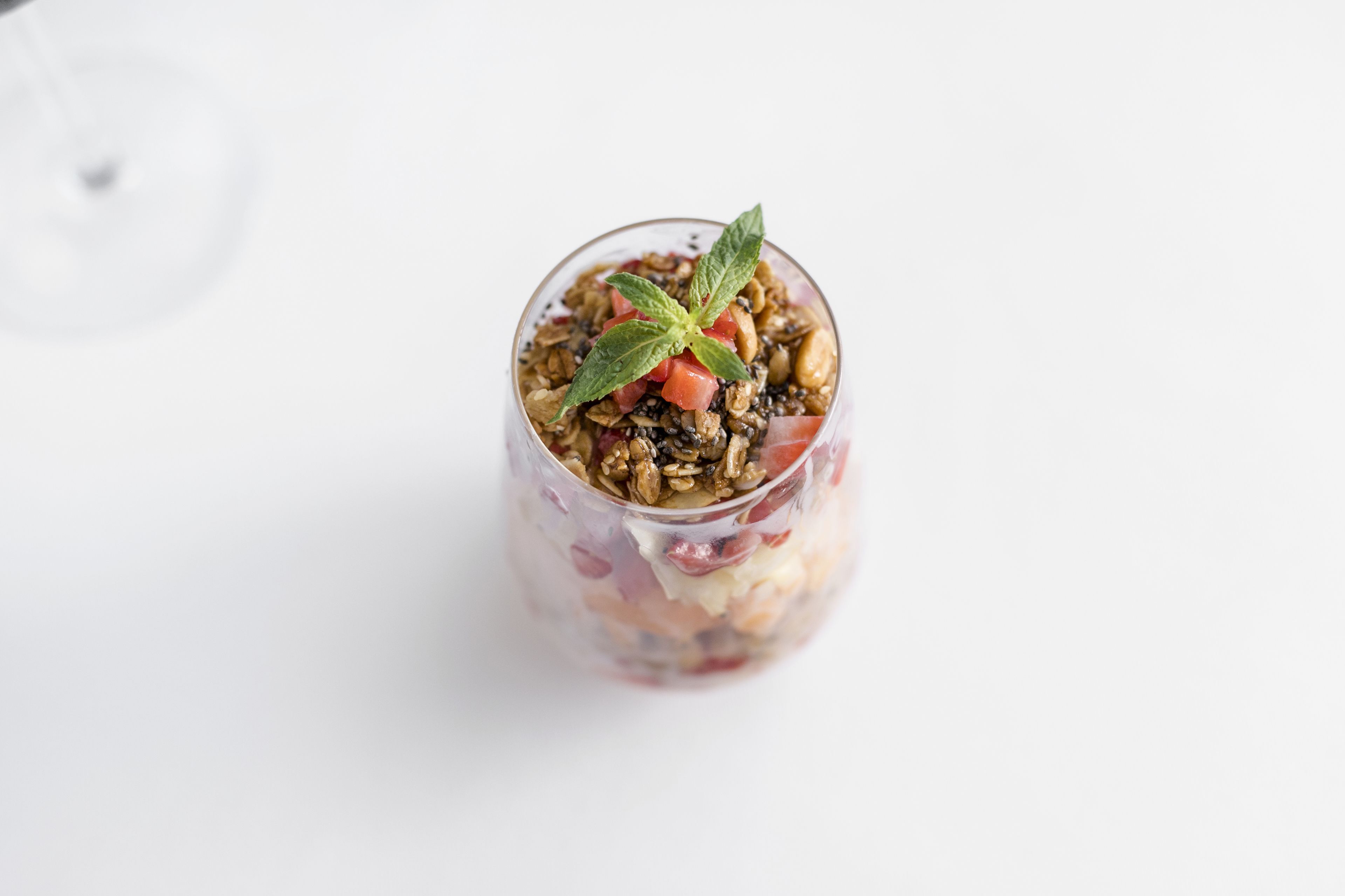 Una copa de vidrio transparente con una ensalada en capas, decorada con una hoja de menta.