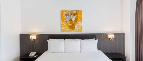 Una habitación de hotel con una cama grande, dos mesitas de noche con lámparas, una obra de arte en la pared y una ventana con cortinas.