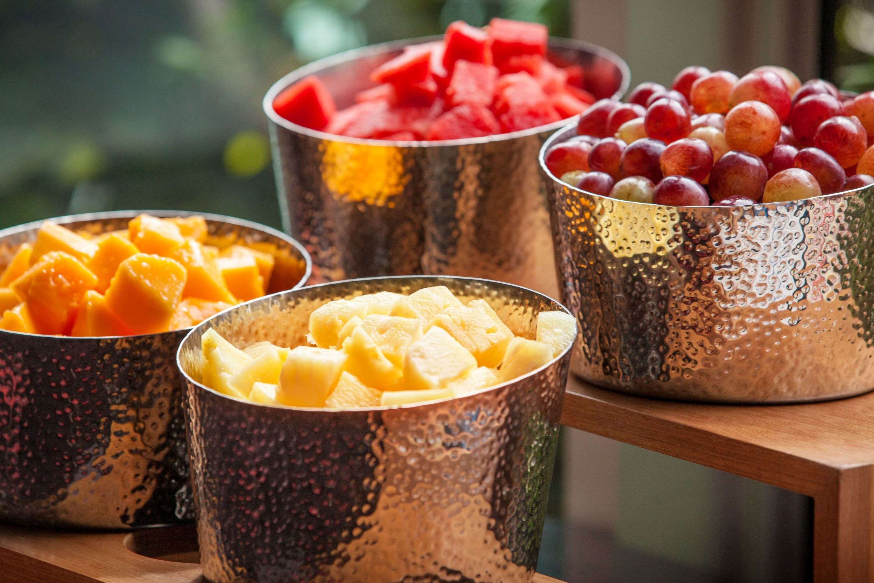 Four metallic bowls filled with various fruits.