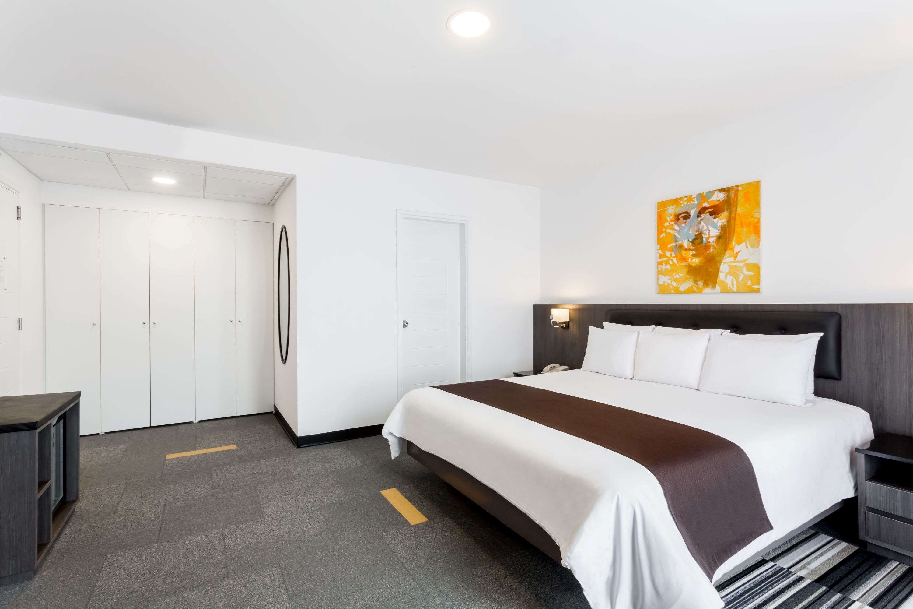 Habitación de hotel con una cama grande, una mesita de noche, un armario y un cuadro en la pared.