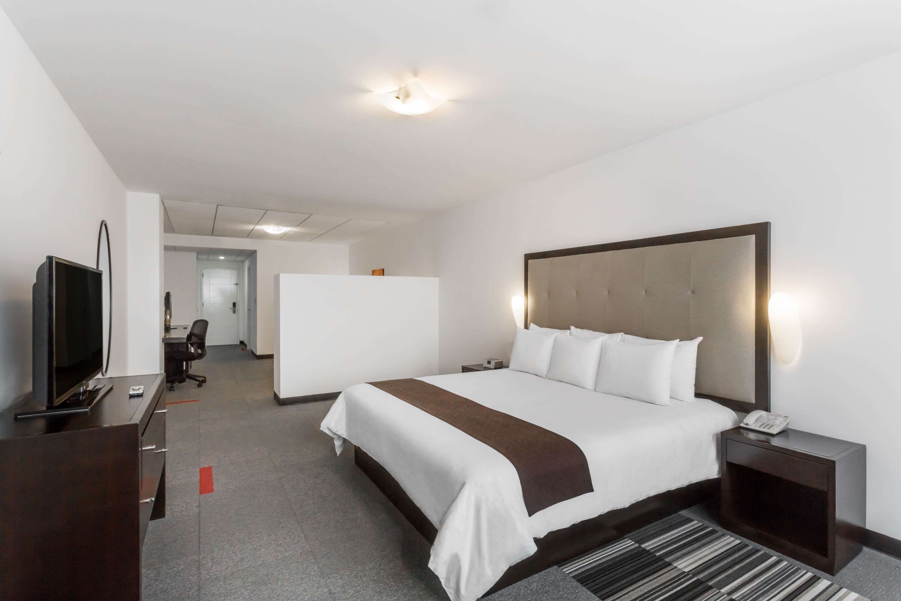 Una habitación de hotel con una cama grande, un televisor en un escritorio, una lámpara de escritorio y un teléfono en una mesita de noche.