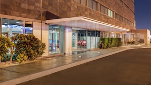 Fachada moderna de hotel con amplios ventanales, un acceso cubierto y un espacio exterior bien cuidado.