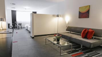 Une chambre d’hôtel moderne avec un canapé gris, une table basse en verre, une lampe sur pied et un tableau au mur.