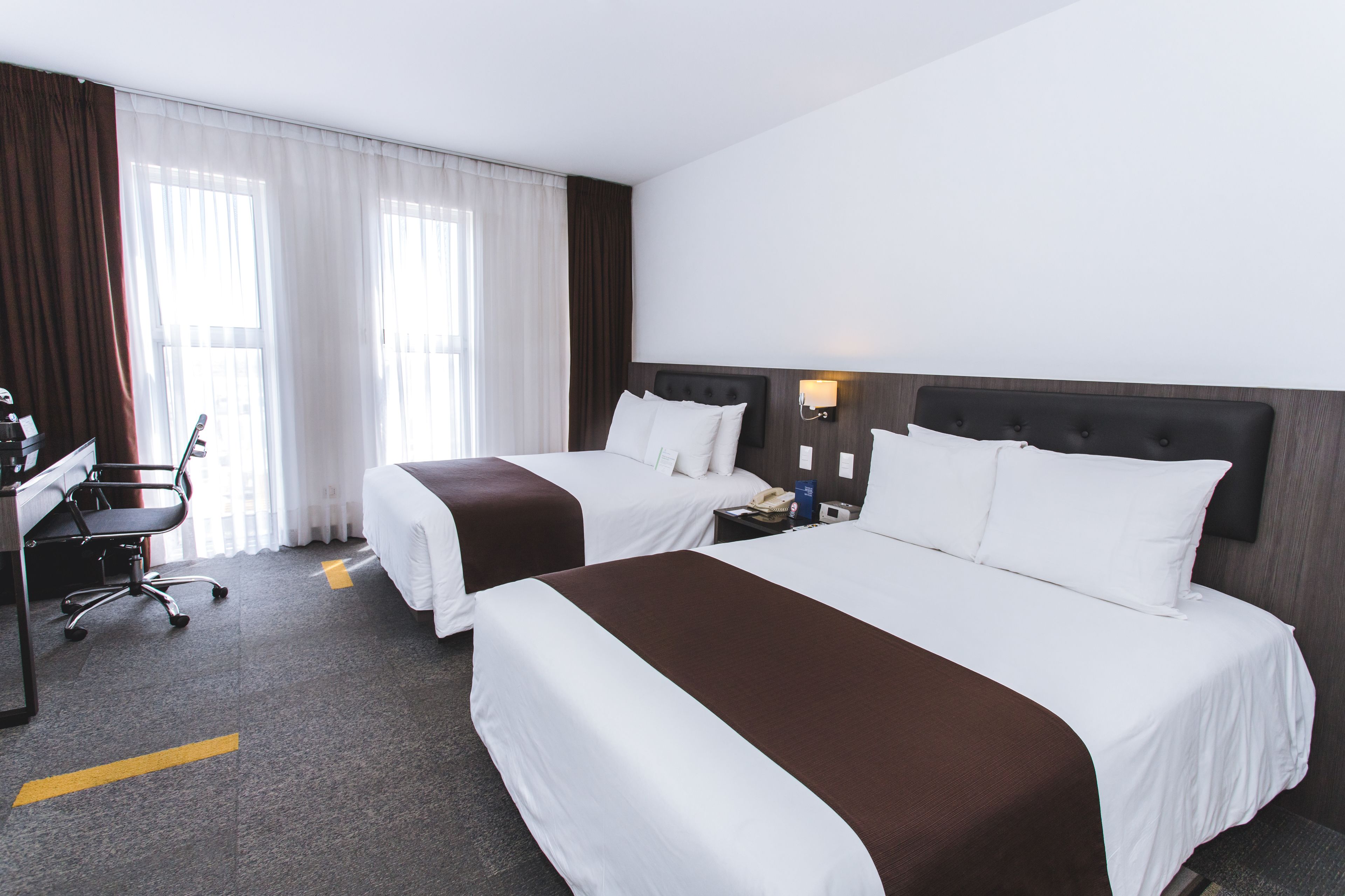 A hotel room with two beds, a desk, and a chair.