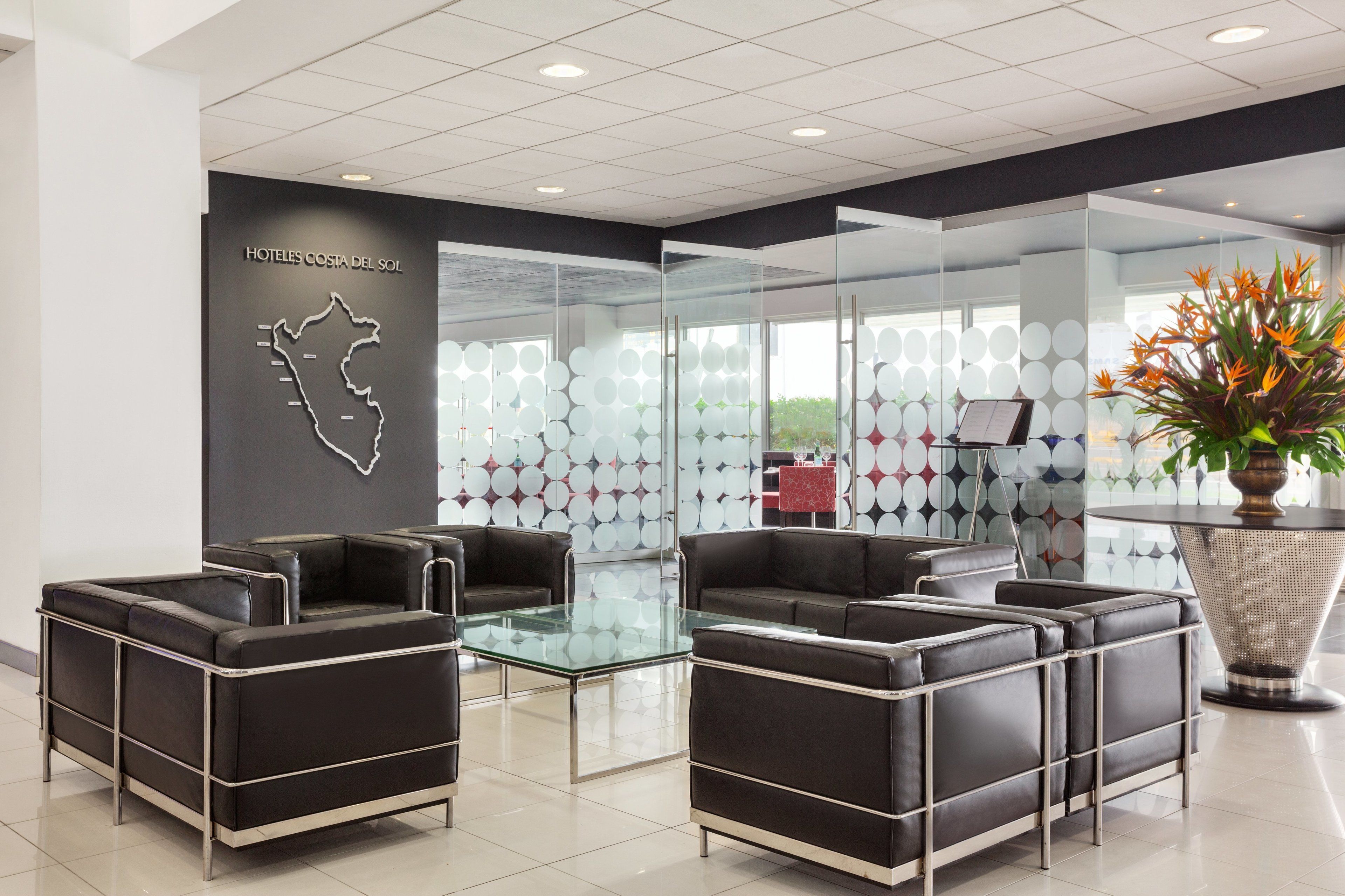 A modern hotel lobby with black leather sofas, a glass table, and a decorative plant.