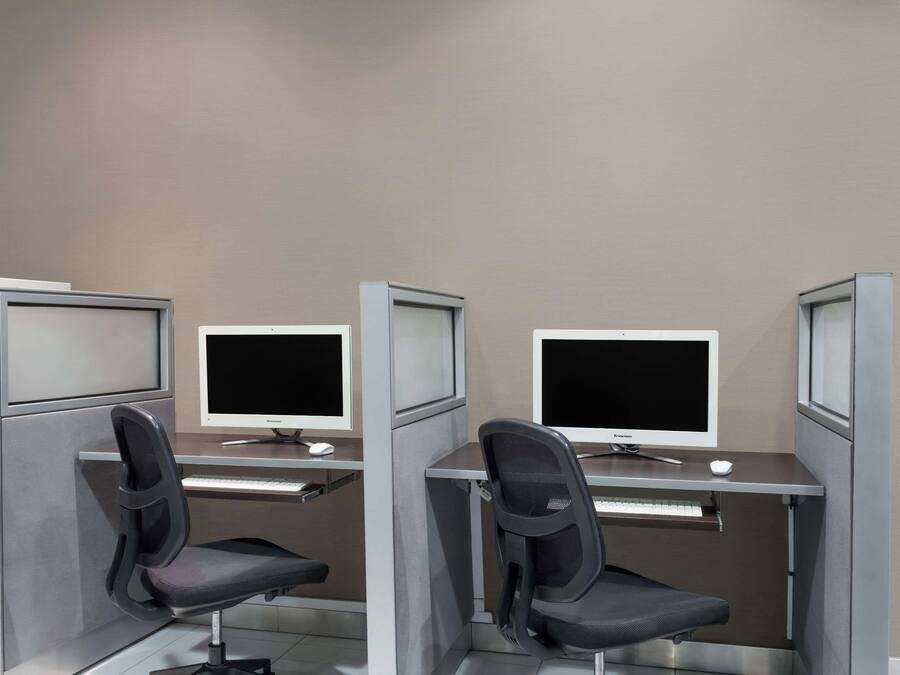A cubicle with two computer desks, each with a monitor and keyboard, and a chair.