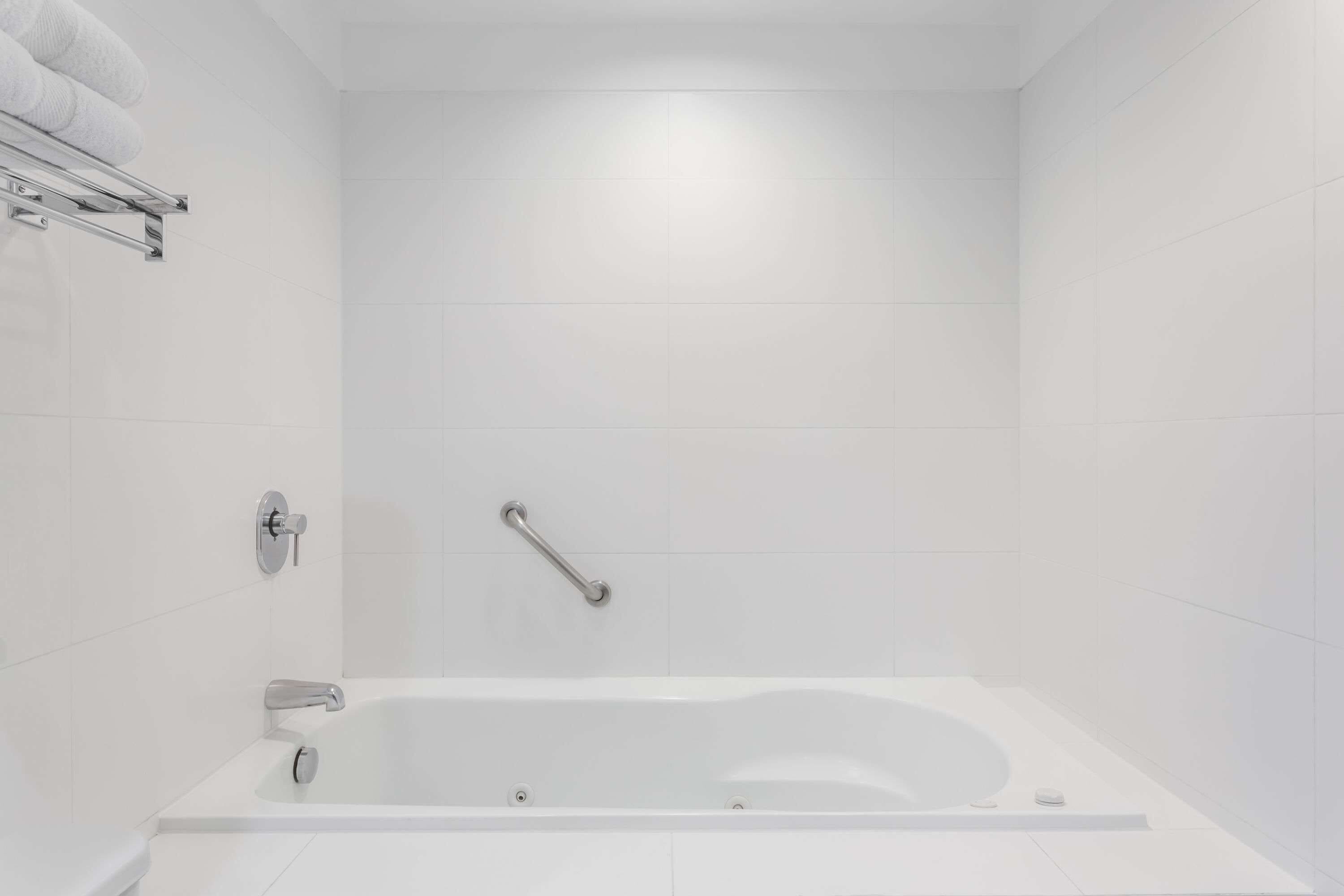 A modern bathroom with a white bathtub, a towel rack, and a grab bar.