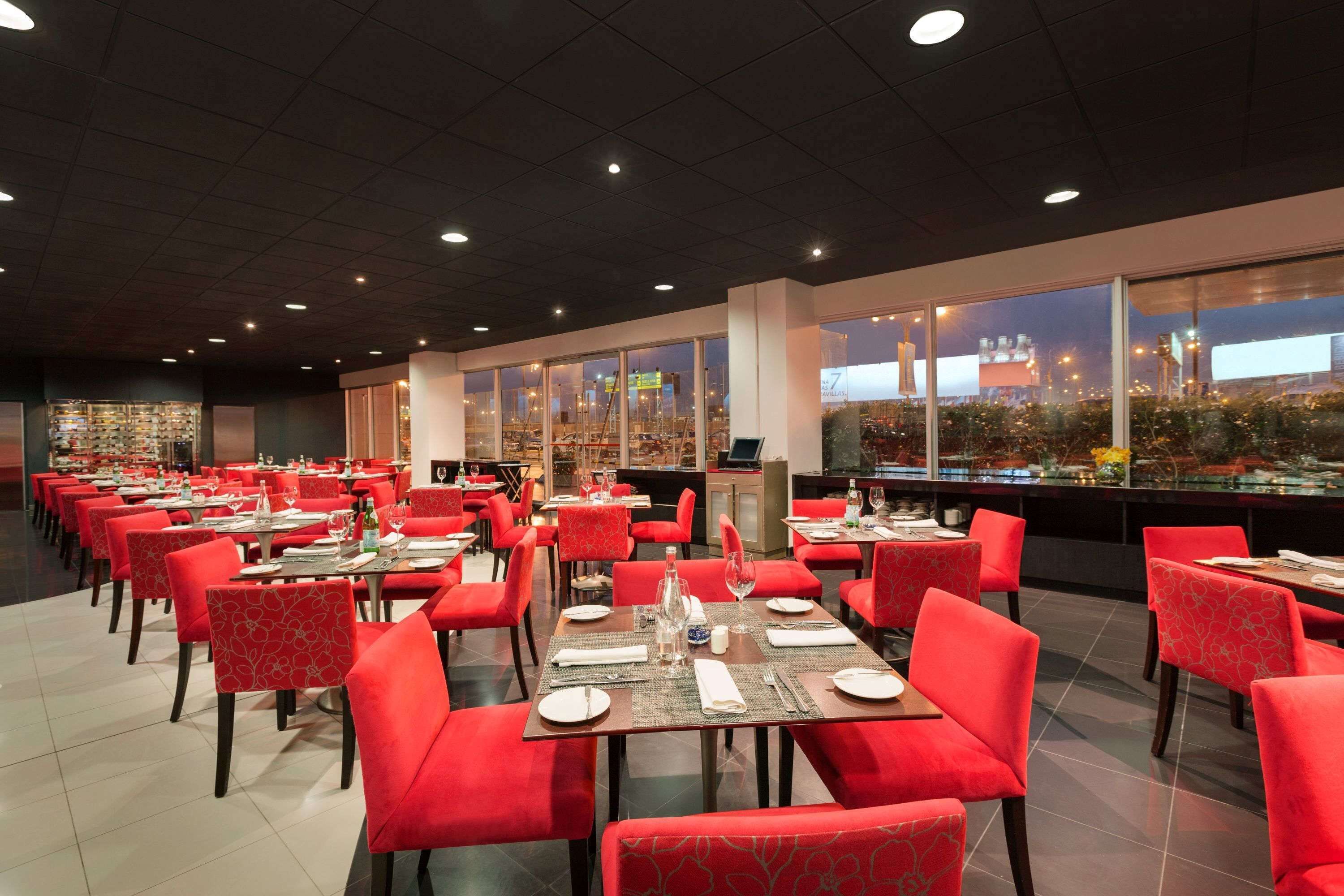Un restaurant spacieux avec des chaises et des tables rouges, de grandes fenêtres offrant une vue sur le paysage urbain.