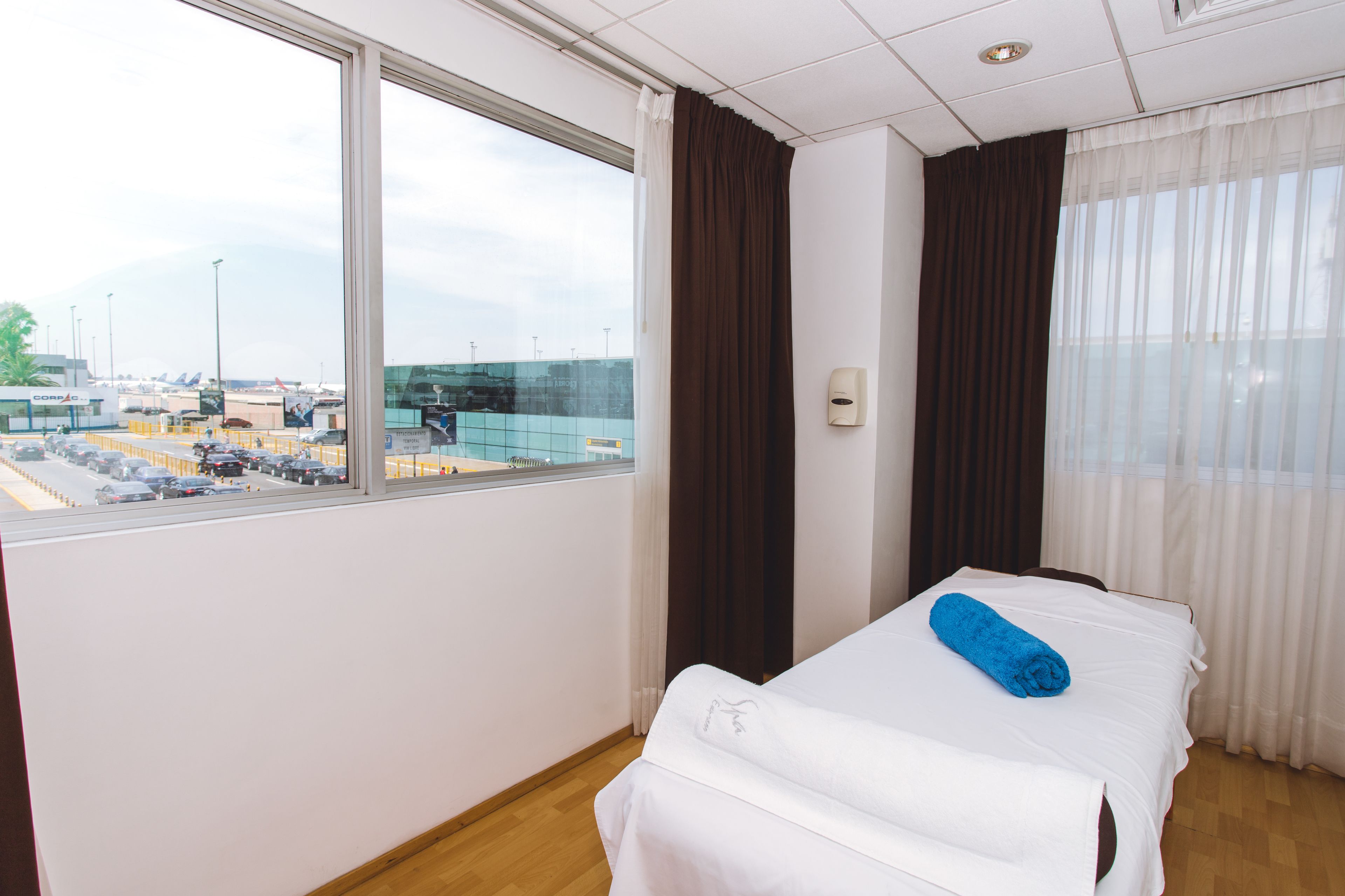 Una habitación de hotel con cama, ventana con vista al aeropuerto y piso de madera.