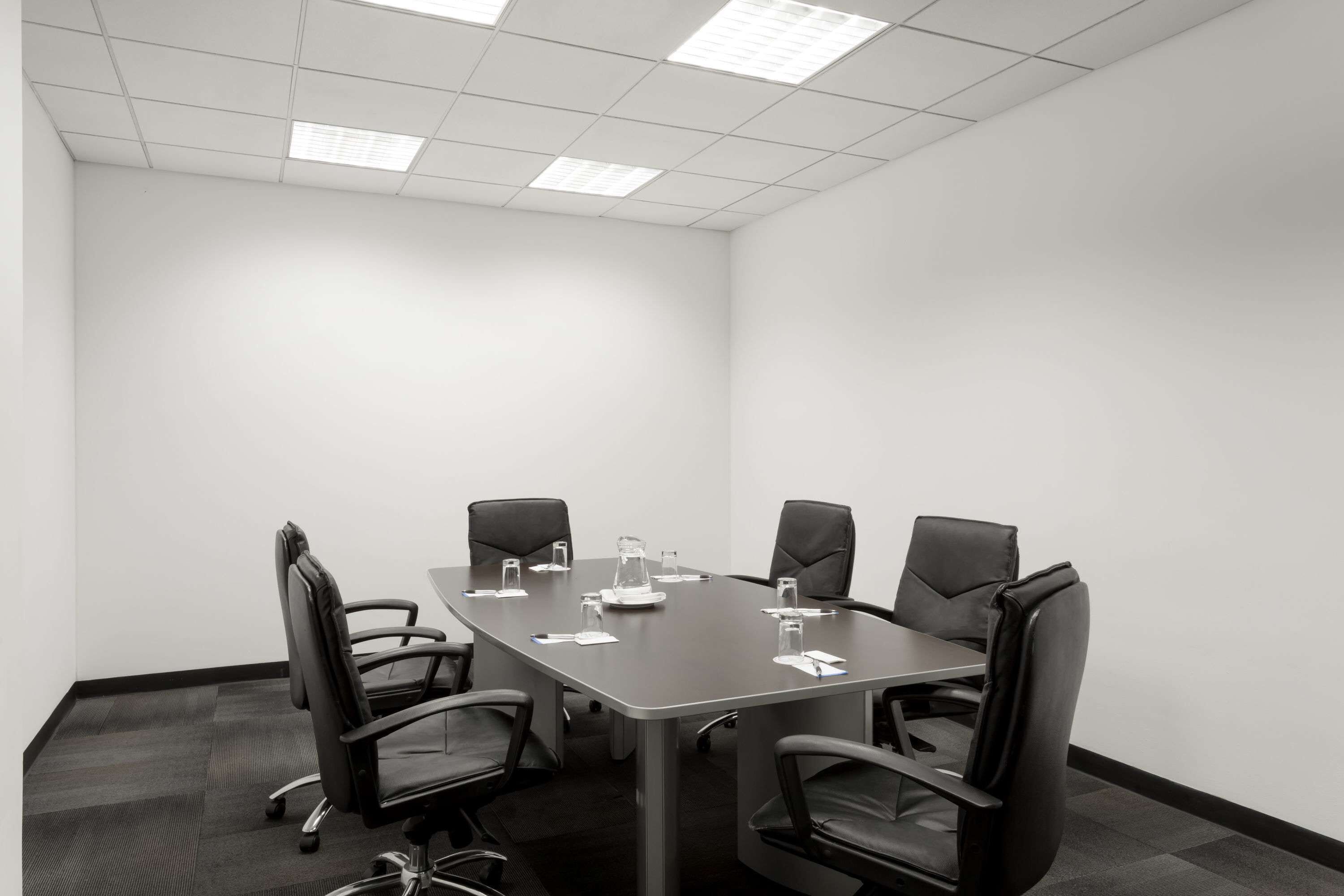 Un salón de conferencias con una mesa rectangular, seis sillas de cuero negro y piso alfombrado.