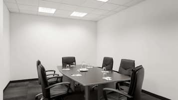 Un salón de conferencias con una mesa rectangular, seis sillas de cuero negro y piso alfombrado.